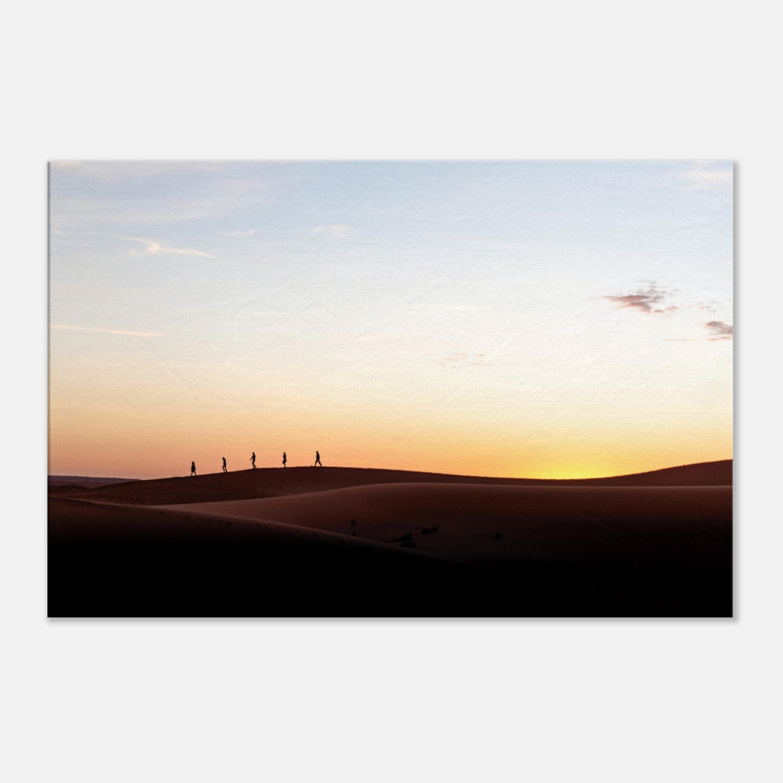Silhouettes of hikers walking across desert dunes at sunset.