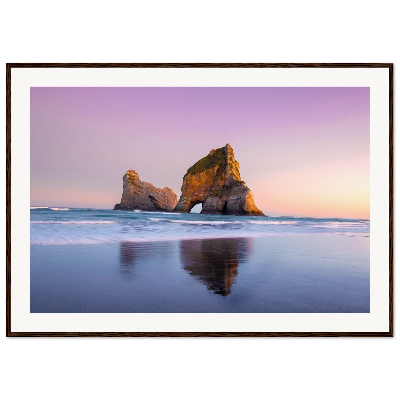 Ocean waves washing over sand beneath a golden sea stack.