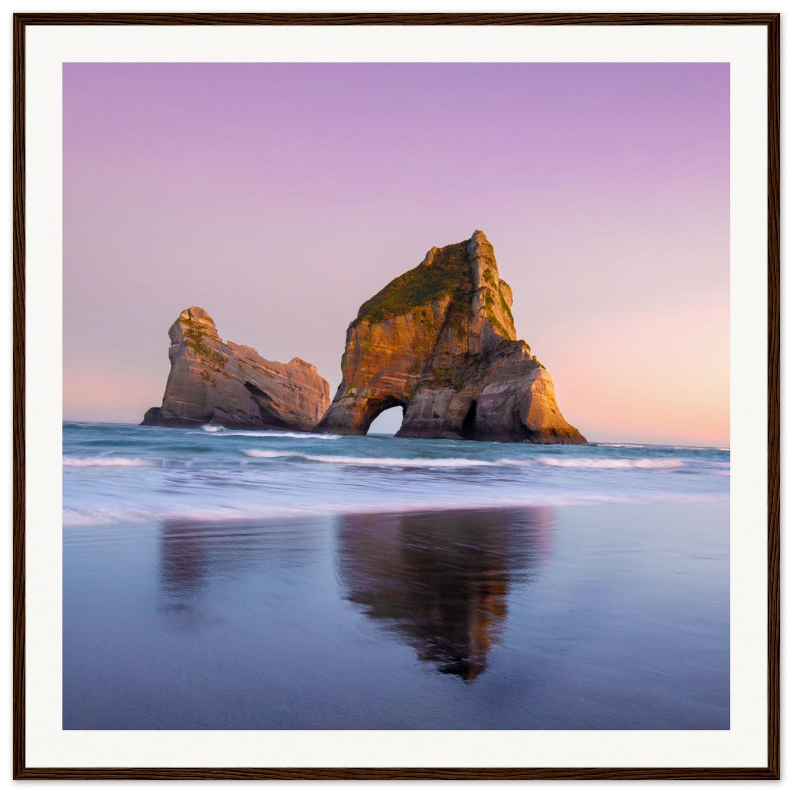 Natural sea arch mirrored in shoreline under pastel sky.