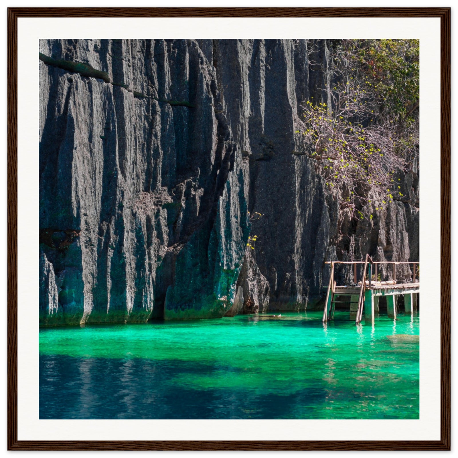 Tropical lagoon with jagged cliffs and a wooden dock in a portrait frame.