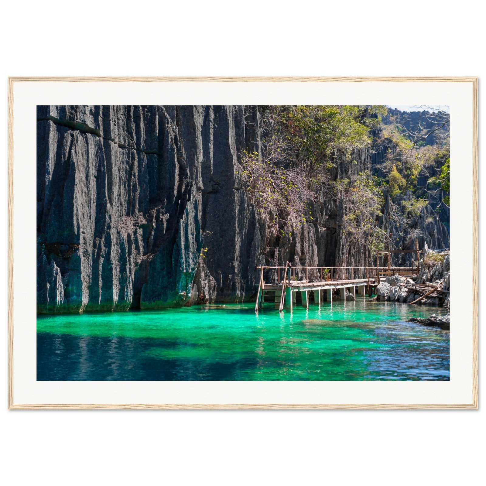 Clear green water at the base of cliffs with a rustic walkway in framed art.

