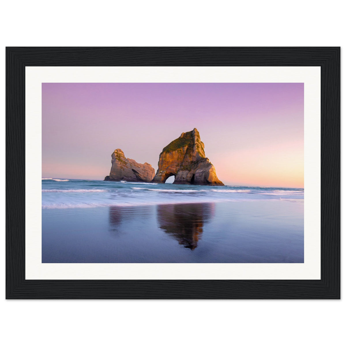 Tranquil sunset beach with wet sand reflecting rock arch.

