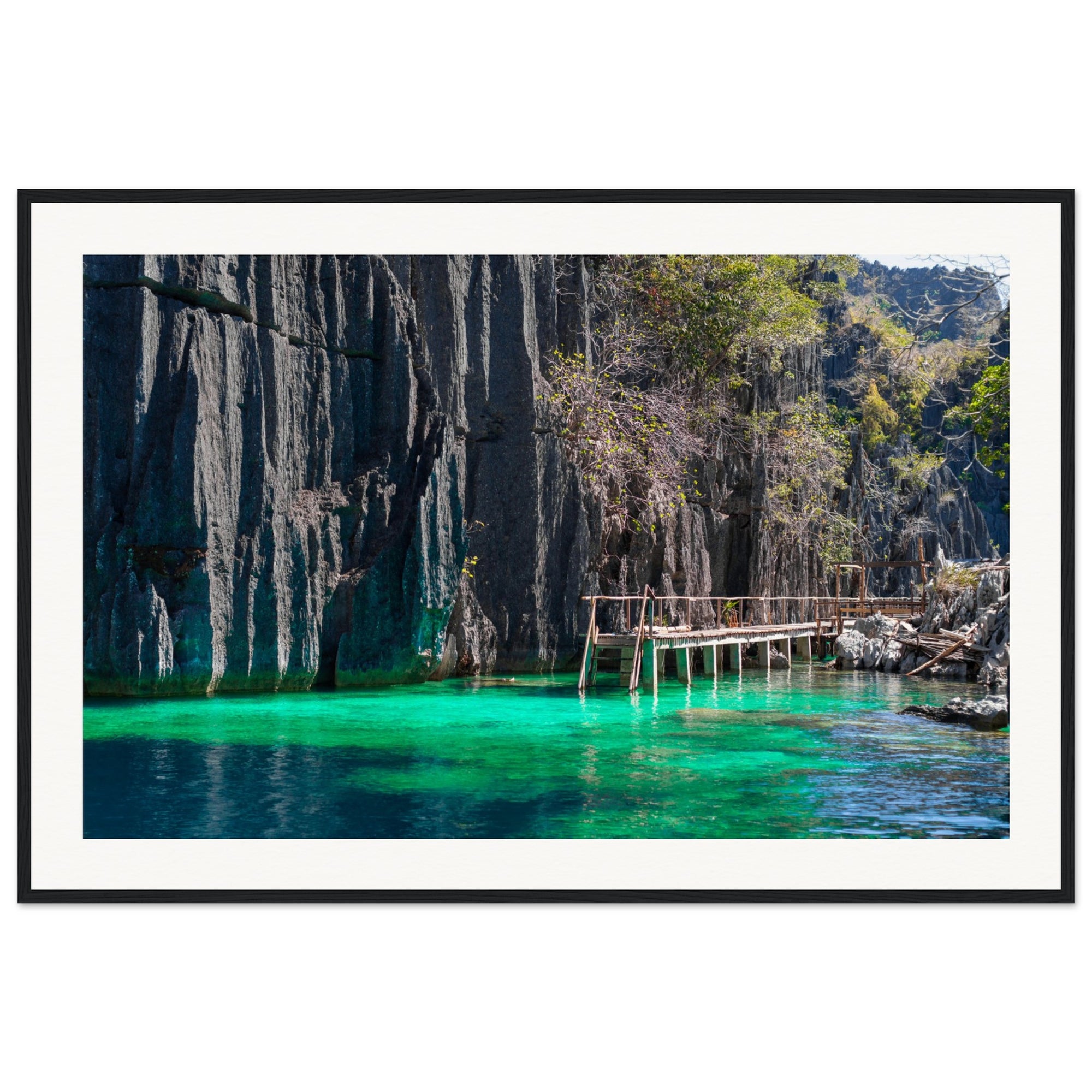 Steep rock face overlooking crystal-clear lagoon in vertical wall art.

