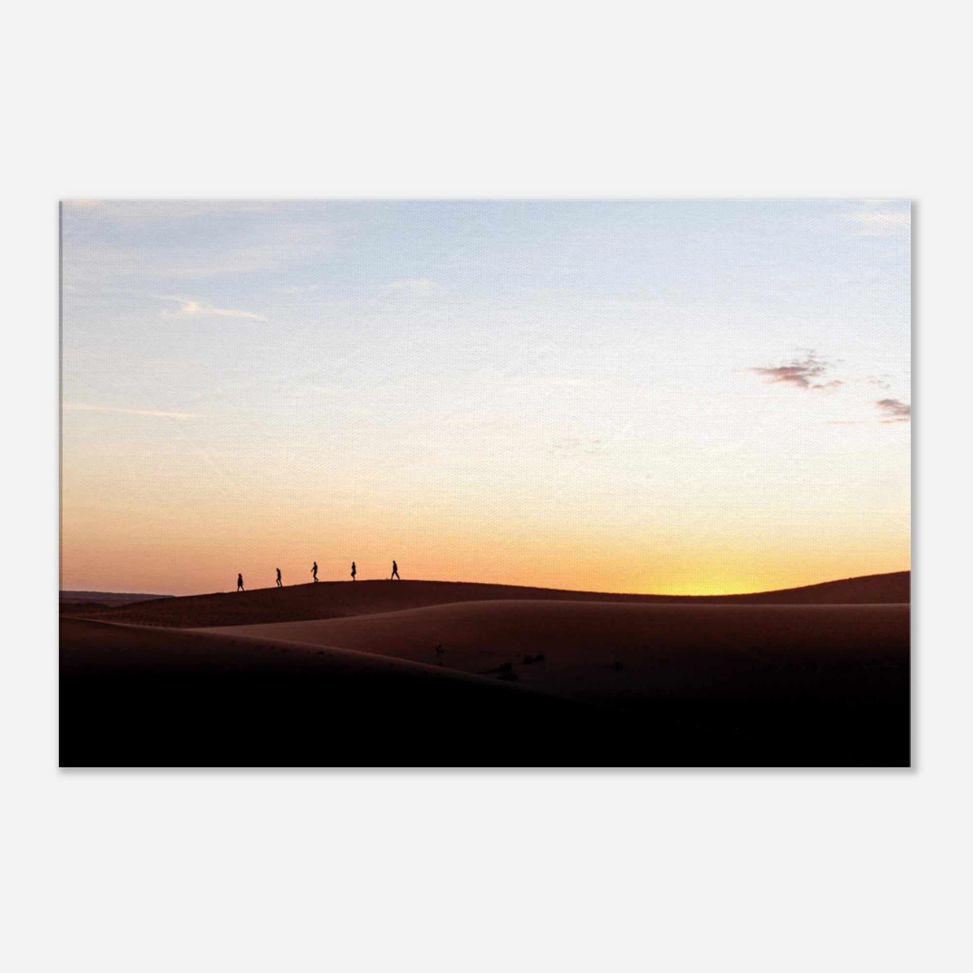 Silhouettes of hikers walking across desert dunes at sunset.

