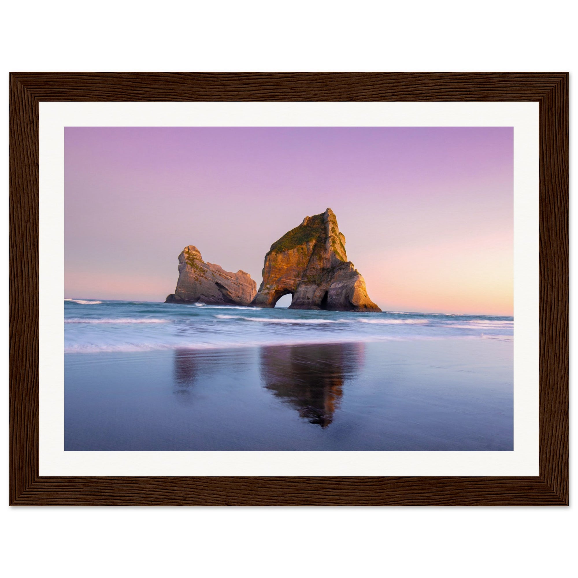 Still waters reflecting rock feature at beach dusk.

