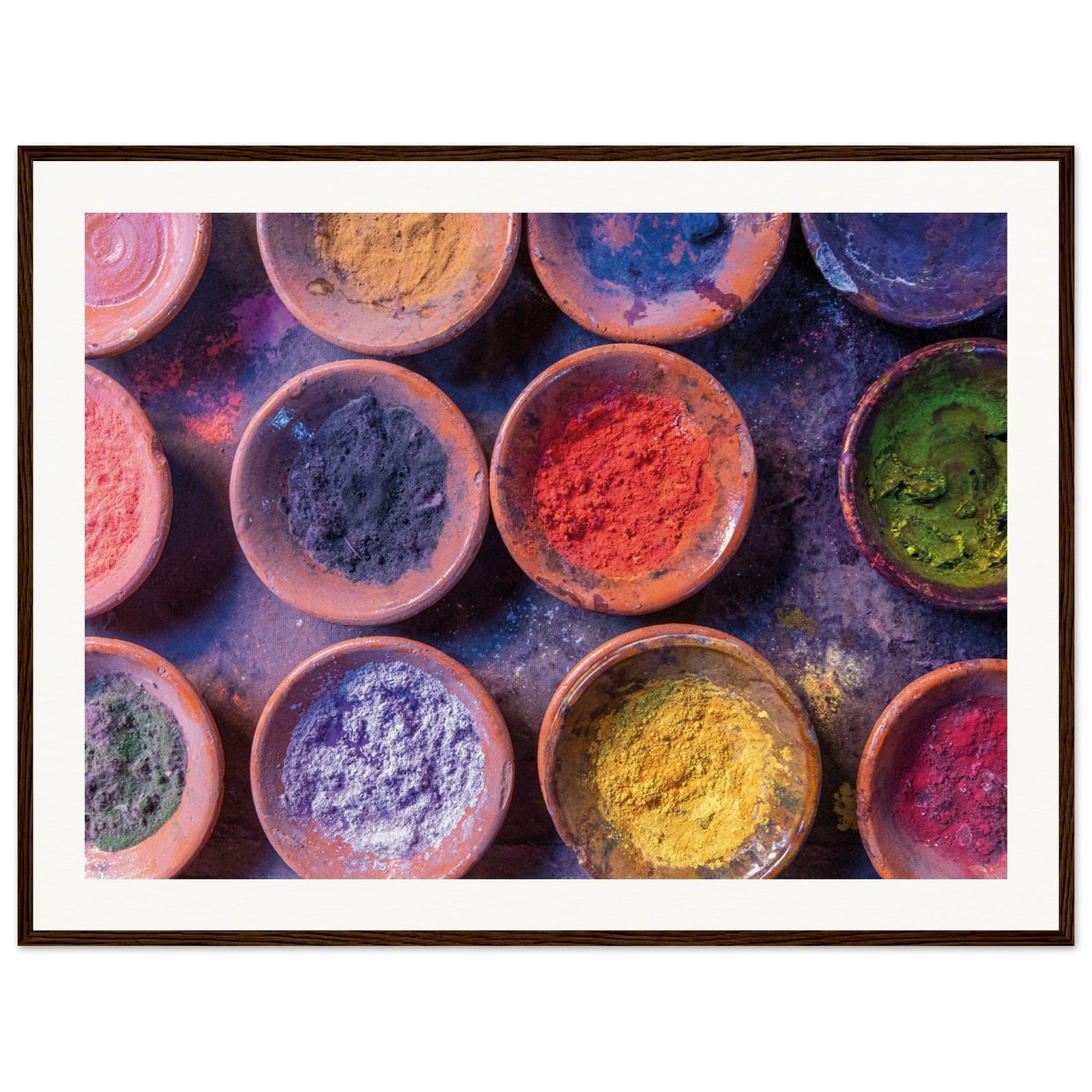 Powder pigments in earthen bowls arranged on a dark surface in a frame.


