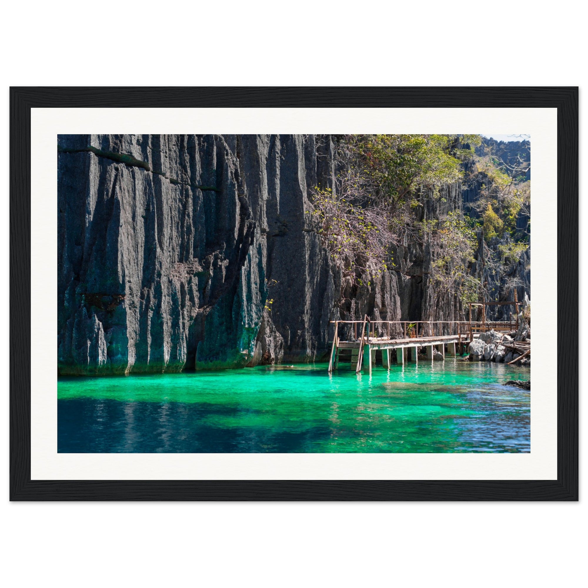 Crystal-clear water beside cliffs with a small bridge in a framed photo.

