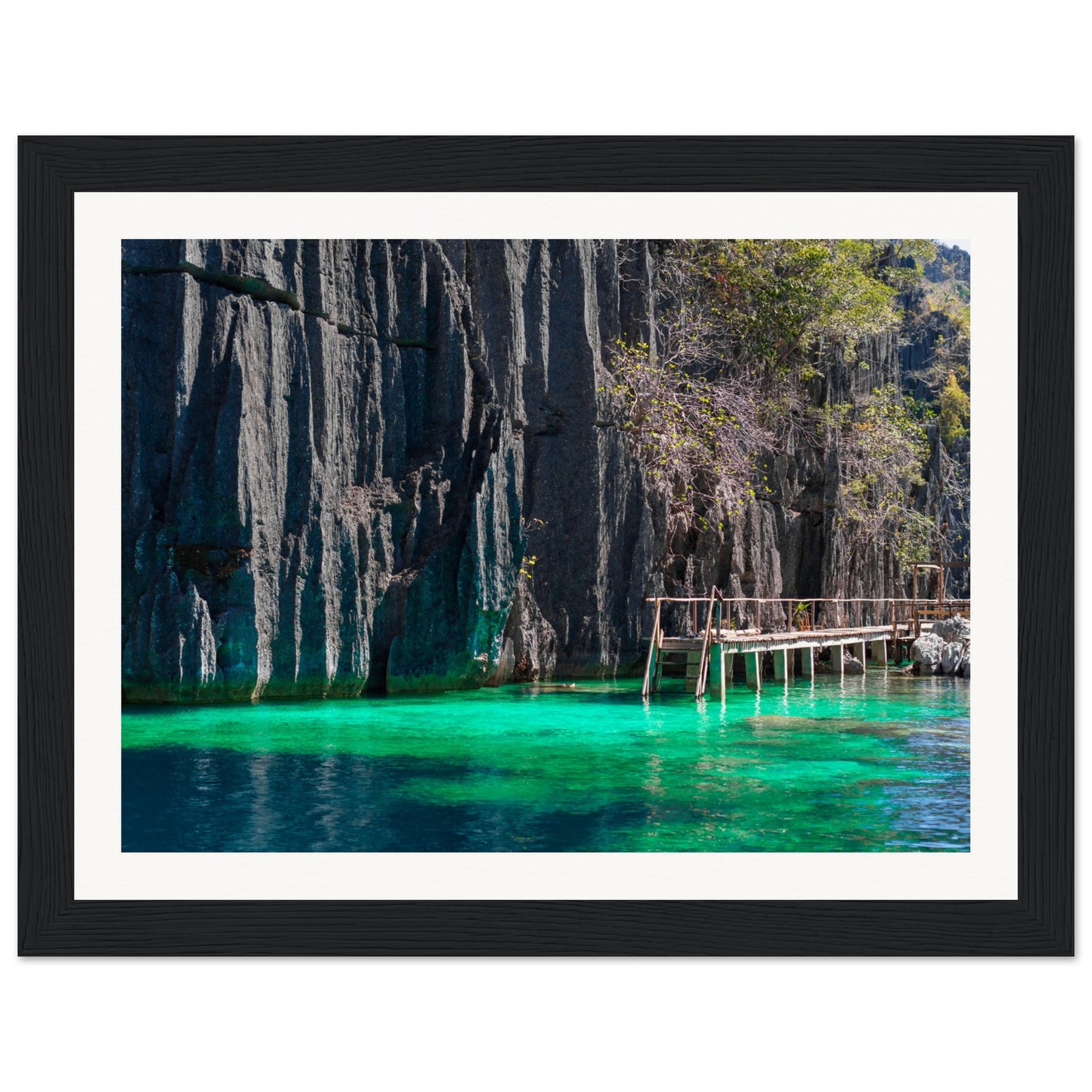 Rustic dock by limestone cliffs above glowing water in framed photo.

