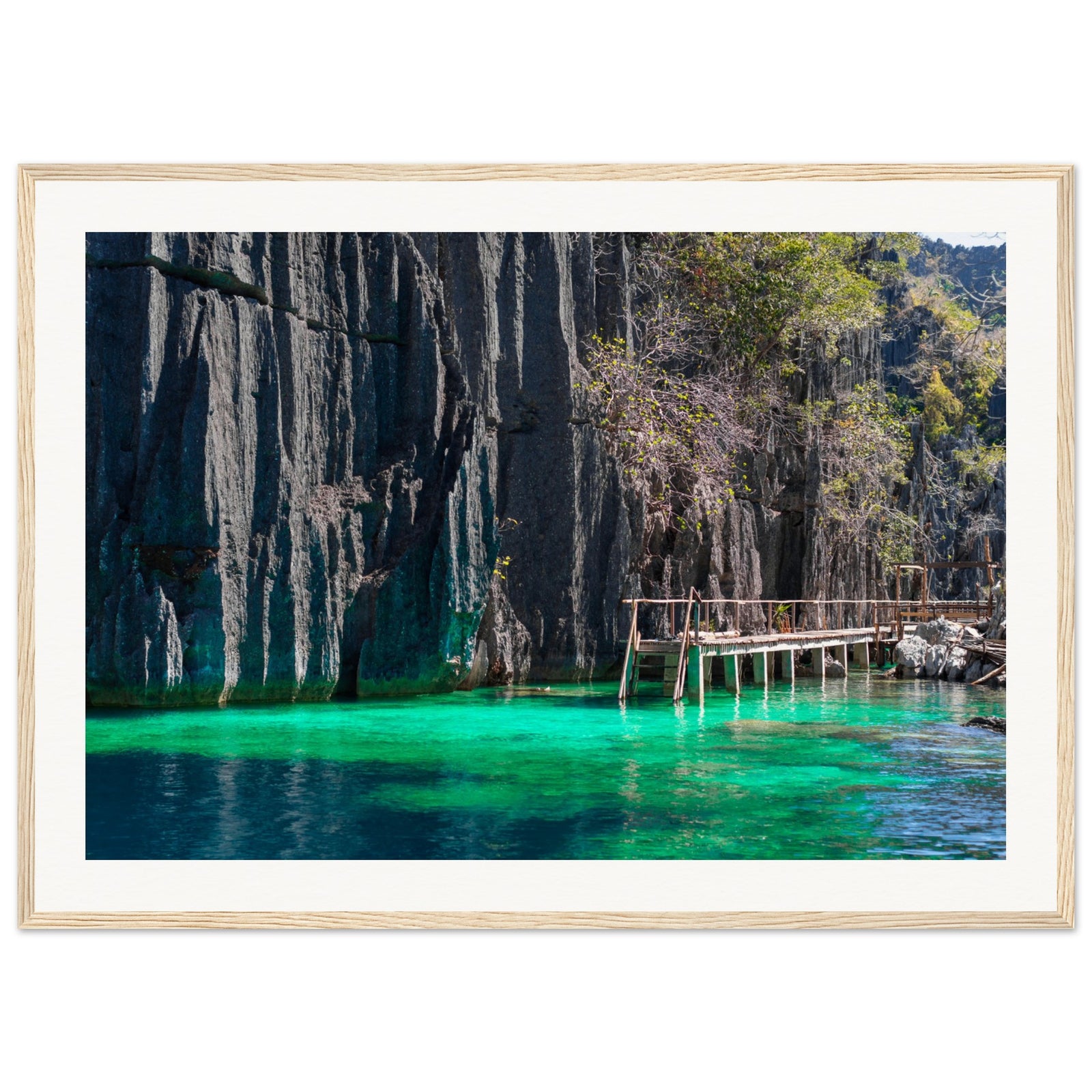 Framed image of steep limestone cliffs and a wooden bridge over blue-green water.

