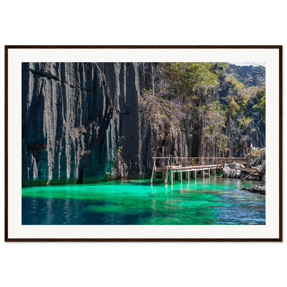 Dock walkway leading through turquoise water in front of cliffs.

