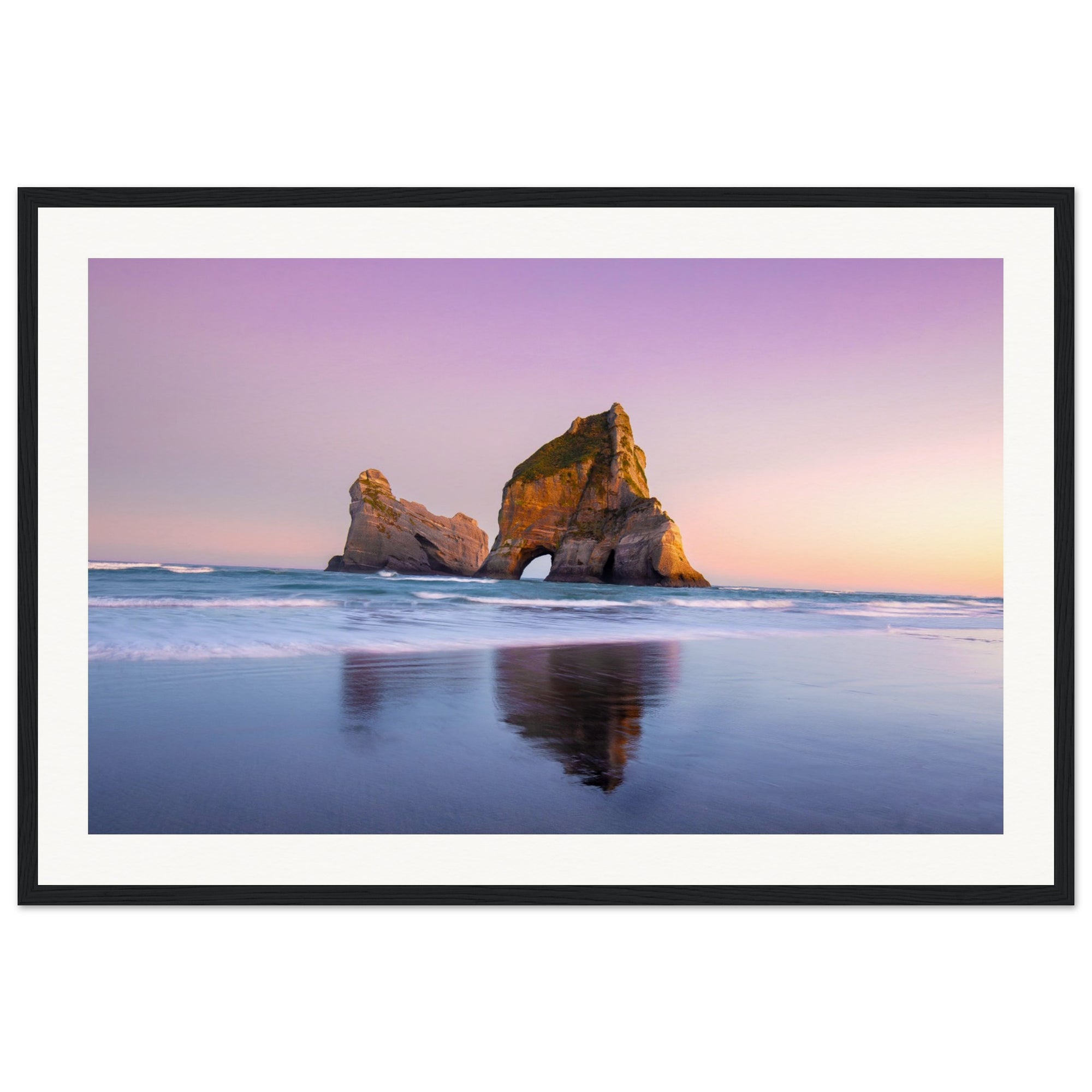 Framed beachscape featuring reflective wet sand and towering rocks.

